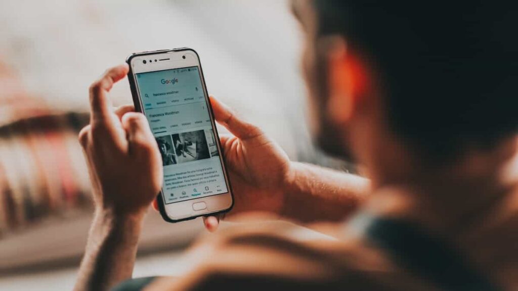 A man is surfing the internet using Google's search engine through his mobile phone